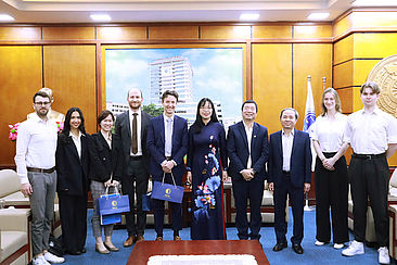 Teil der Reisegruppe in förmlicher Kleidung posiert in einem Raum gemeinsam mit Vertretern der Rechtshochschule Hanoi für ein Gruppenfoto